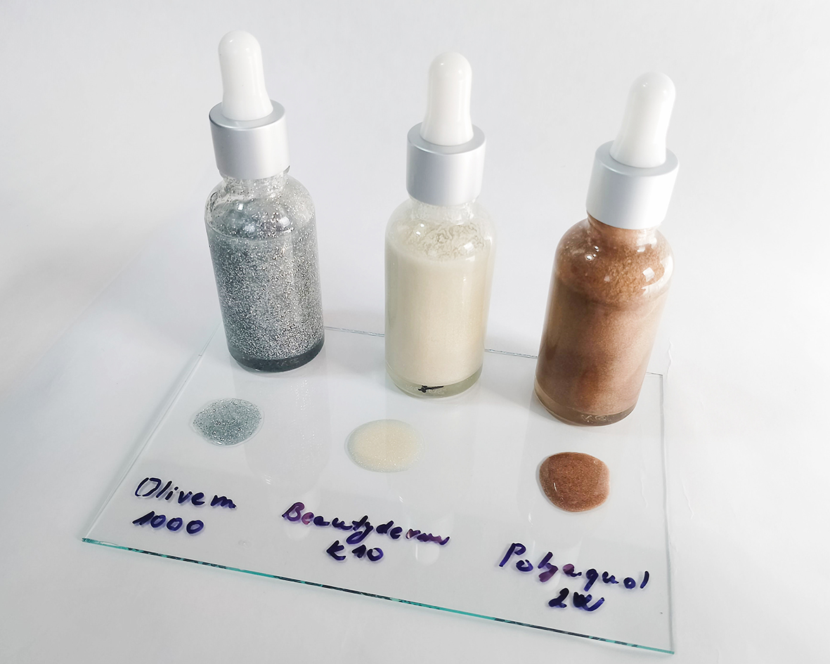 Tre tipi di oli liquidi scintillanti immediatamente dopo la miscelazione in flaconi in vetro con contagocce. Flaconi, piastra acrilica trasparente con gocce di oli su sfondo bianco.